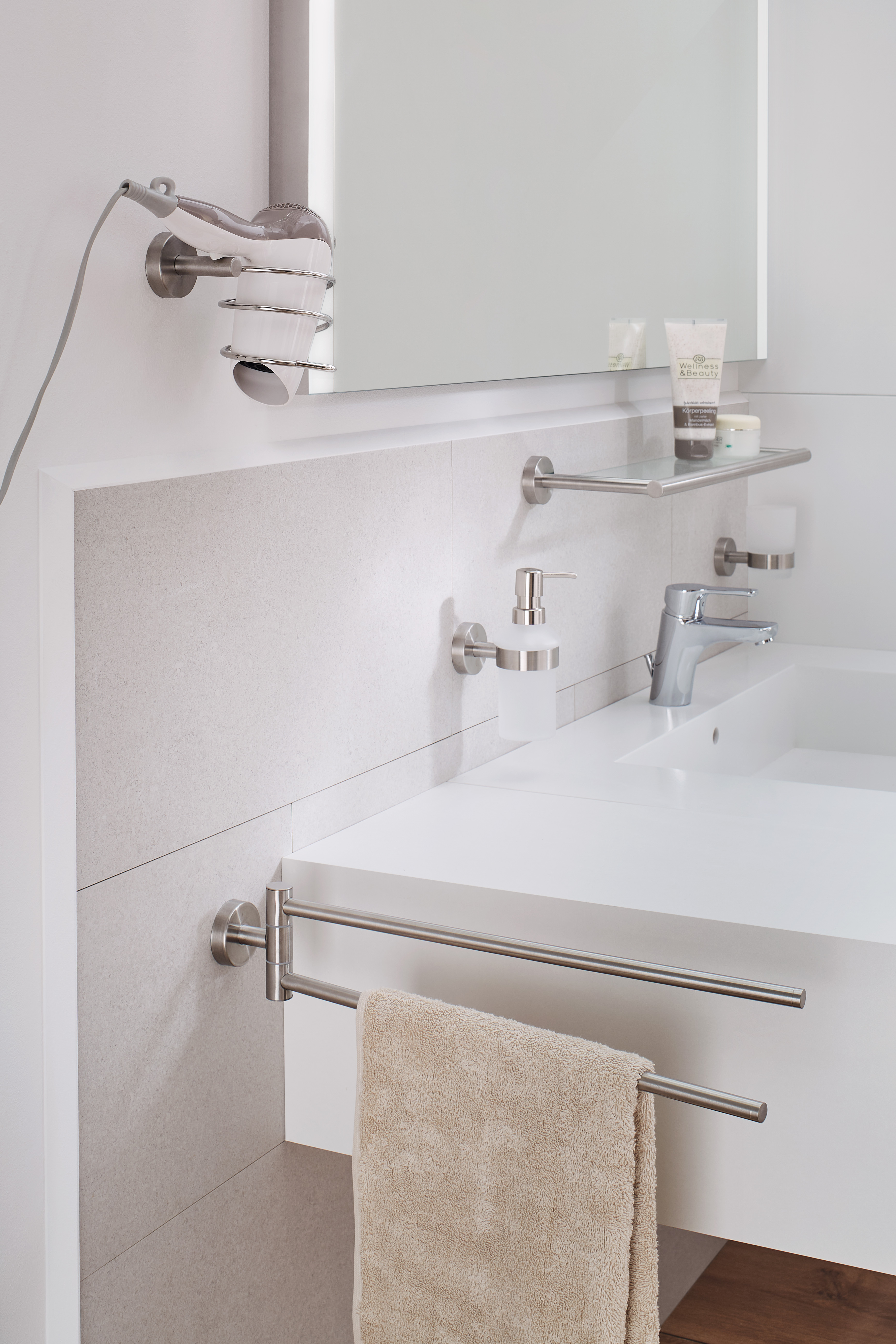Modernes Badezimmer mit Edelstahl-Accessoires, Handtuchhalter, Seifenspender und Fönhalter an einer weißen Wand.