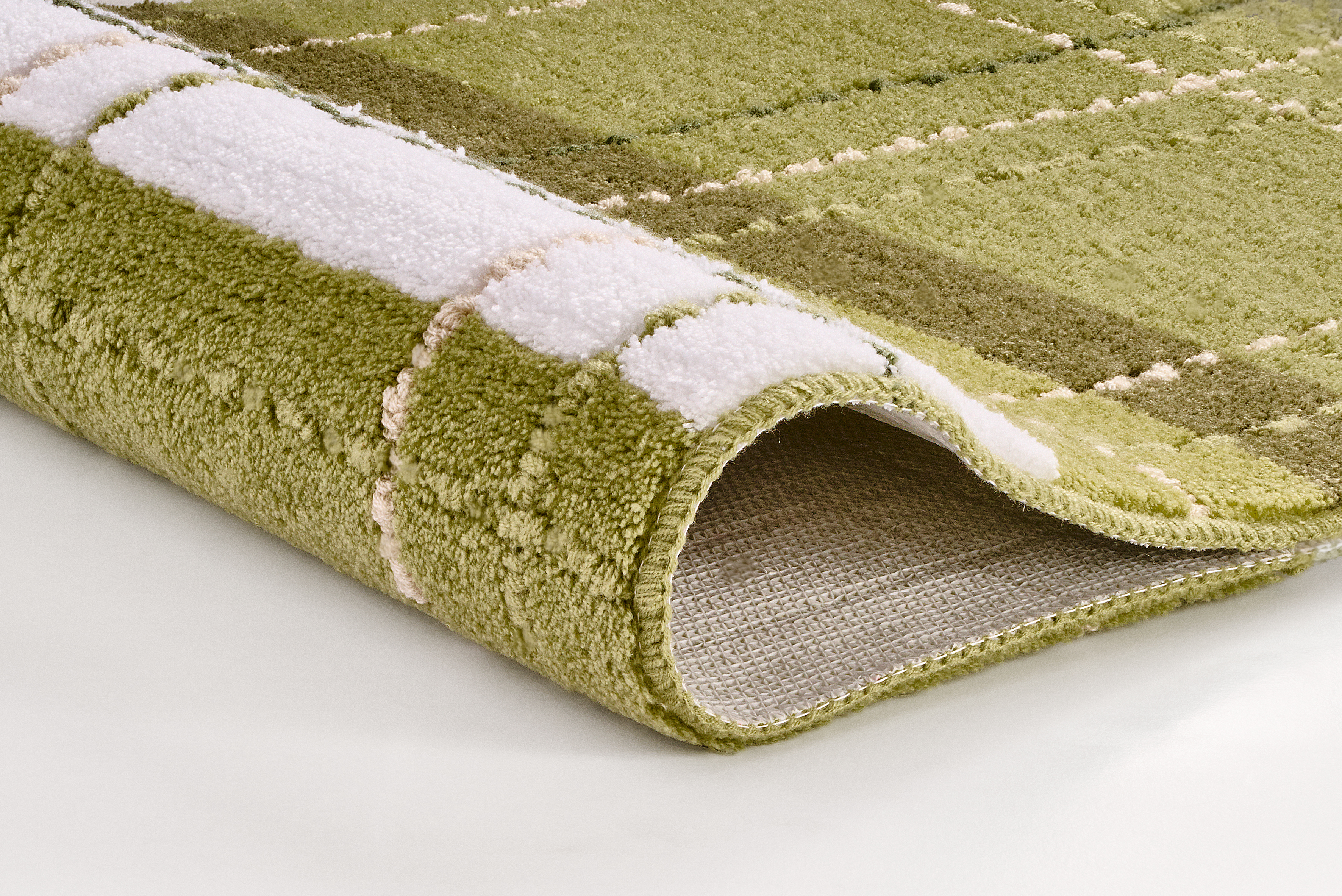 Grüner Teppich mit kariertem Muster in verschiedenen Grüntönen und Weiß, weiche Textur, aufgerollte Ecke zeigt Rückseite.