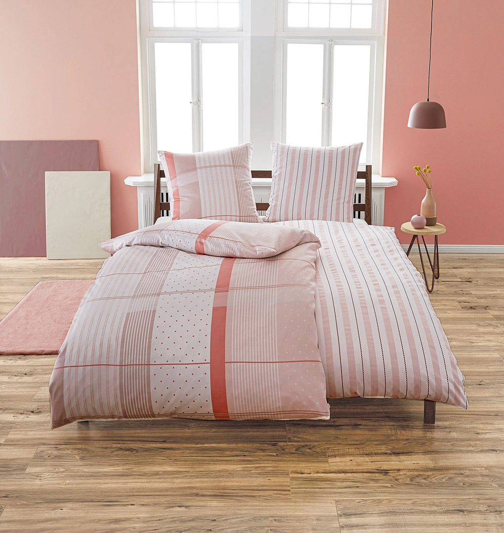 Bettwäsche-Set in Rosa mit Streifen- und Punktmuster, dekoriert in modernem Schlafzimmer mit Holzboden und rosa Wänden.