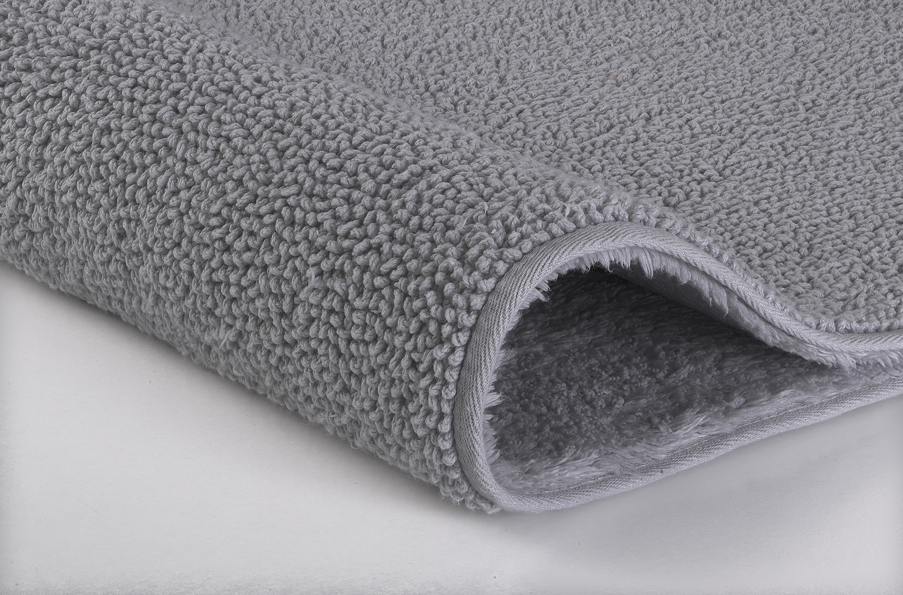 Grauer, flauschiger Badteppich mit weicher, strukturierter Oberfläche und abgerundeten Kanten. Ideal für ein gemütliches Badezimmer.