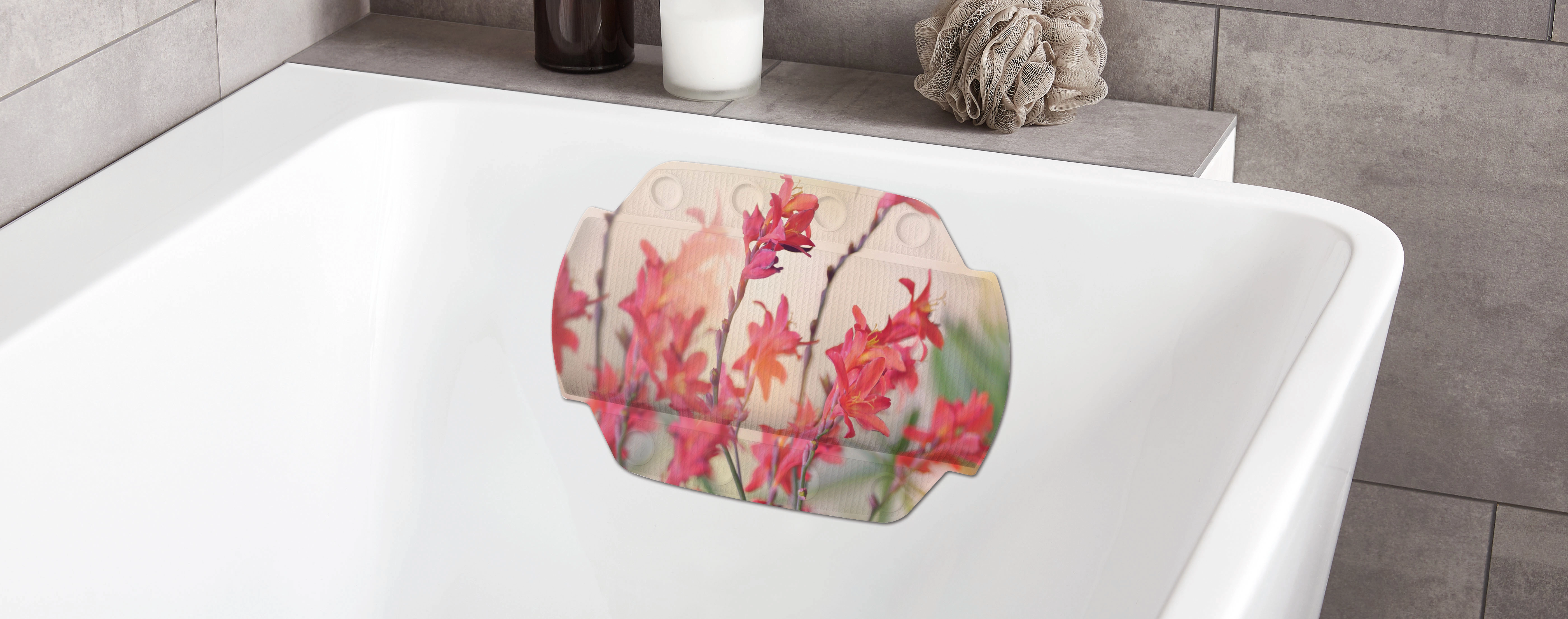 Badezimmer mit weißer Badewanne und bunter Badematte mit Kolibri- und Blumenmotiv, dekoriert mit Kerze und Schwamm.