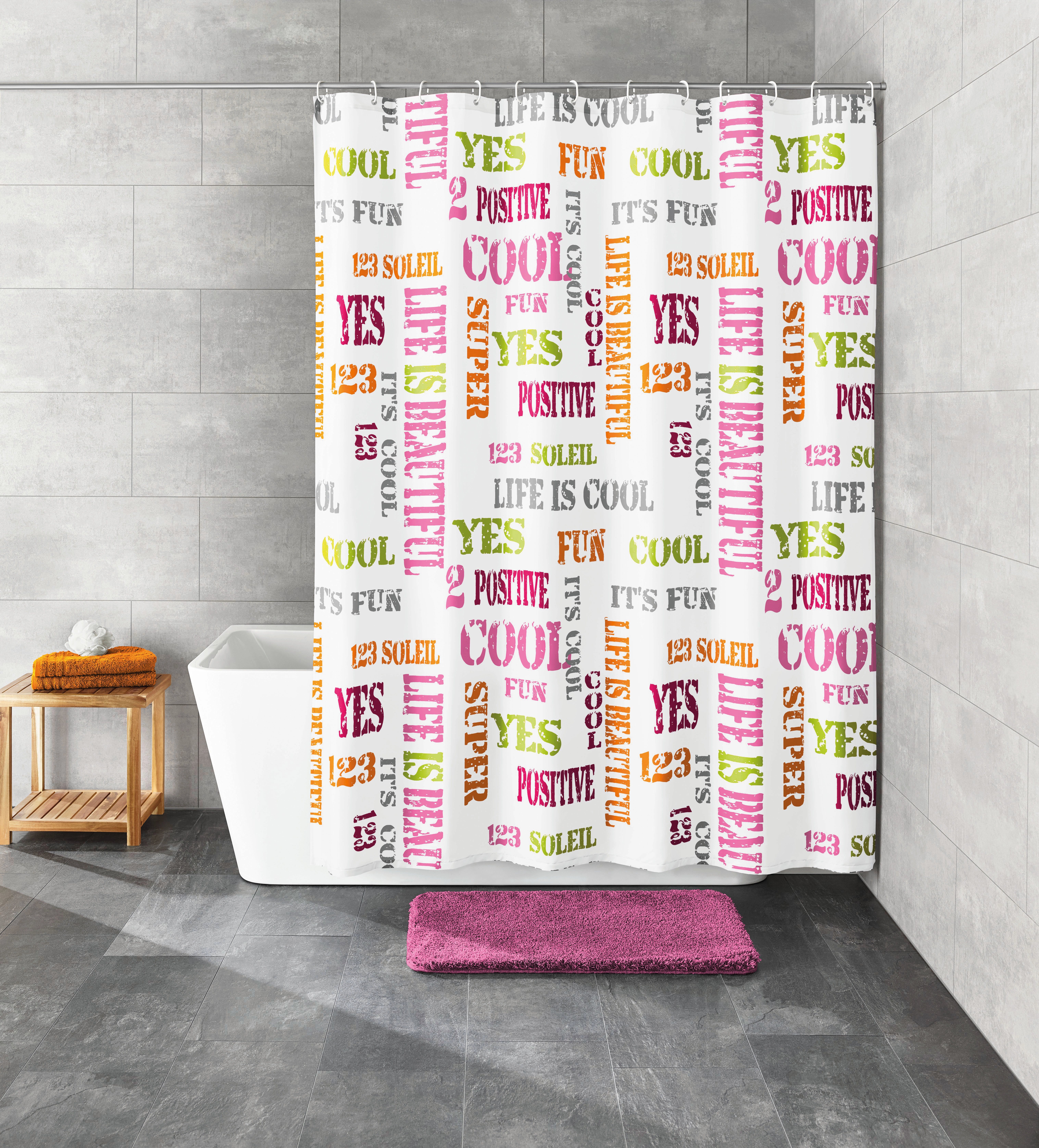 Duschvorhang mit bunten Schriftzügen in modernem Badezimmer, graue Fliesen, Badewanne, Holzregal und lila Badematte.