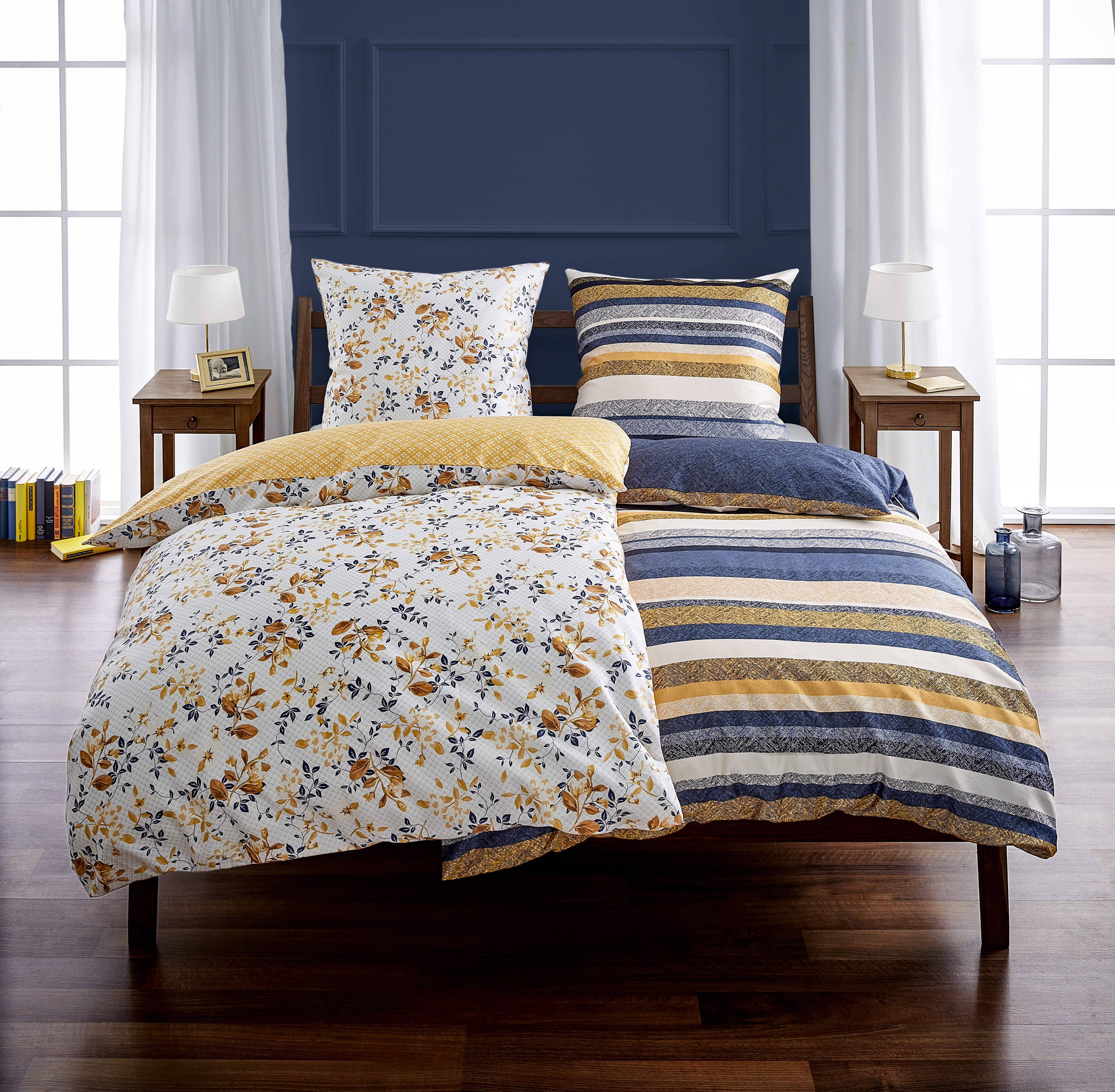 Bettwäsche-Set mit floralem und gestreiftem Design in Blau, Gelb und Weiß, auf einem Bett in modernem Schlafzimmer.