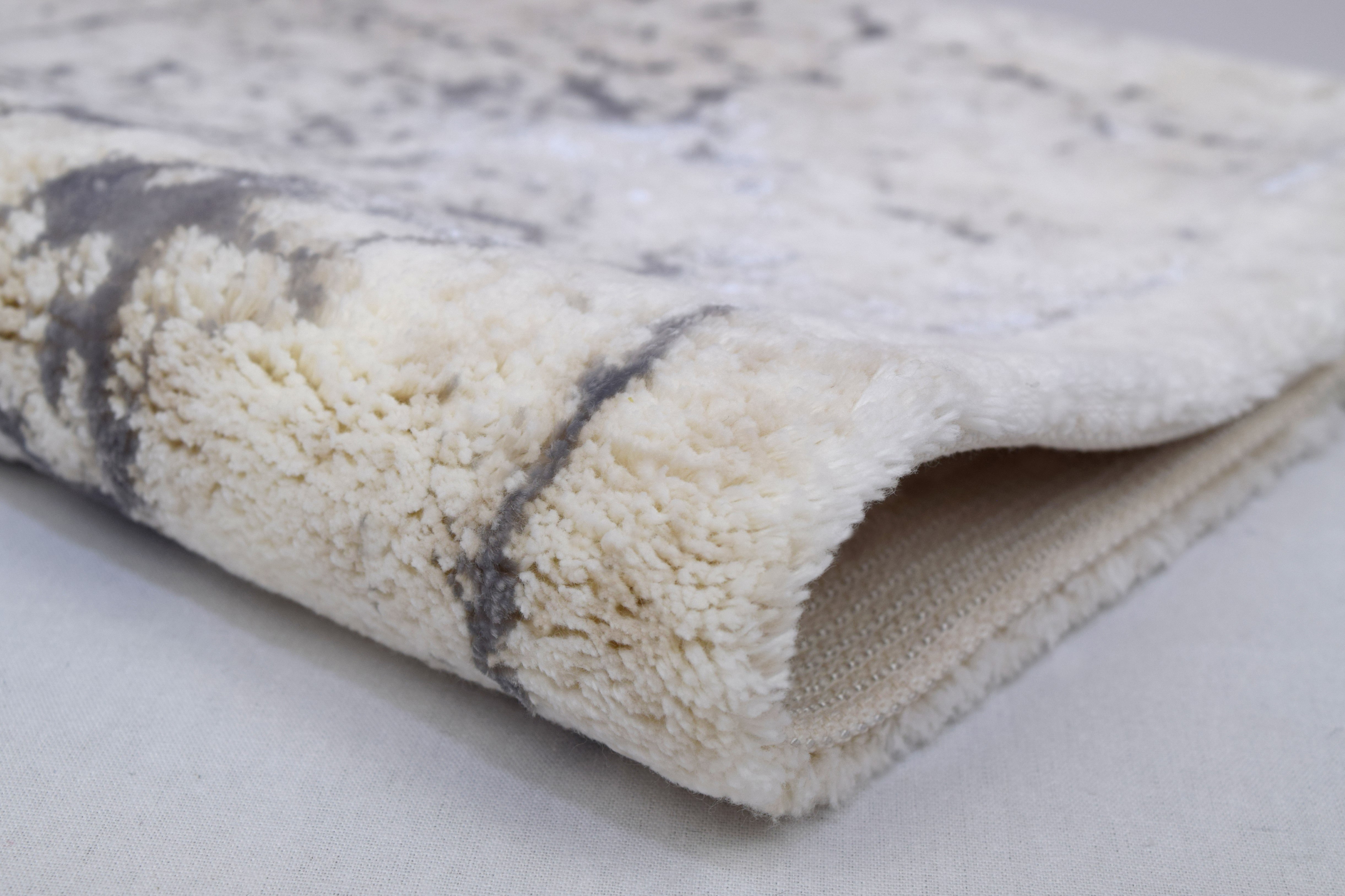 Weicher, cremefarbener Teppich mit grauen Akzenten, flauschige Textur, ideal für gemütliche Wohnräume.