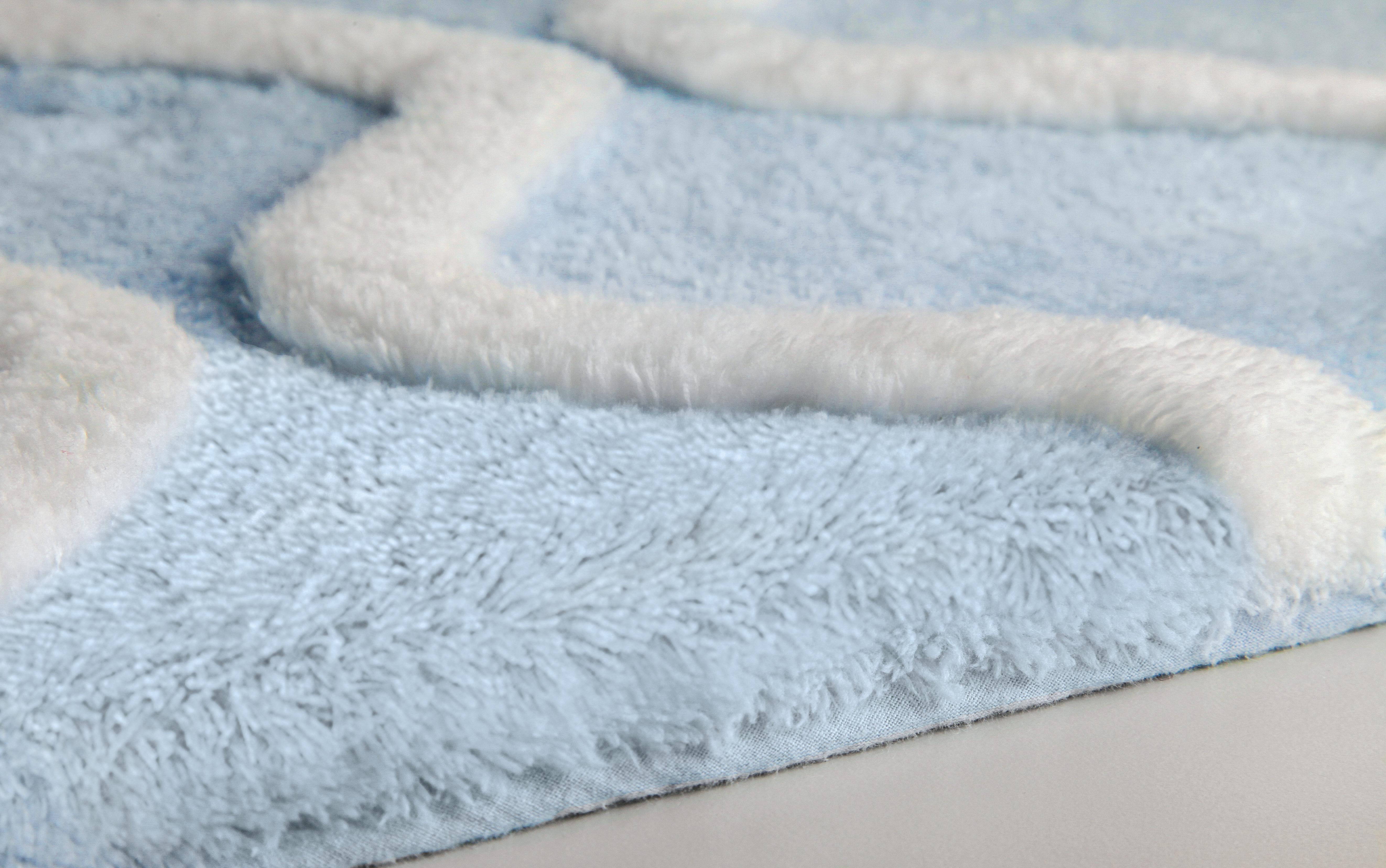 Weicher, hellblauer Badteppich mit weißem, geometrischem Muster und flauschiger Oberfläche für ein gemütliches Badezimmer.