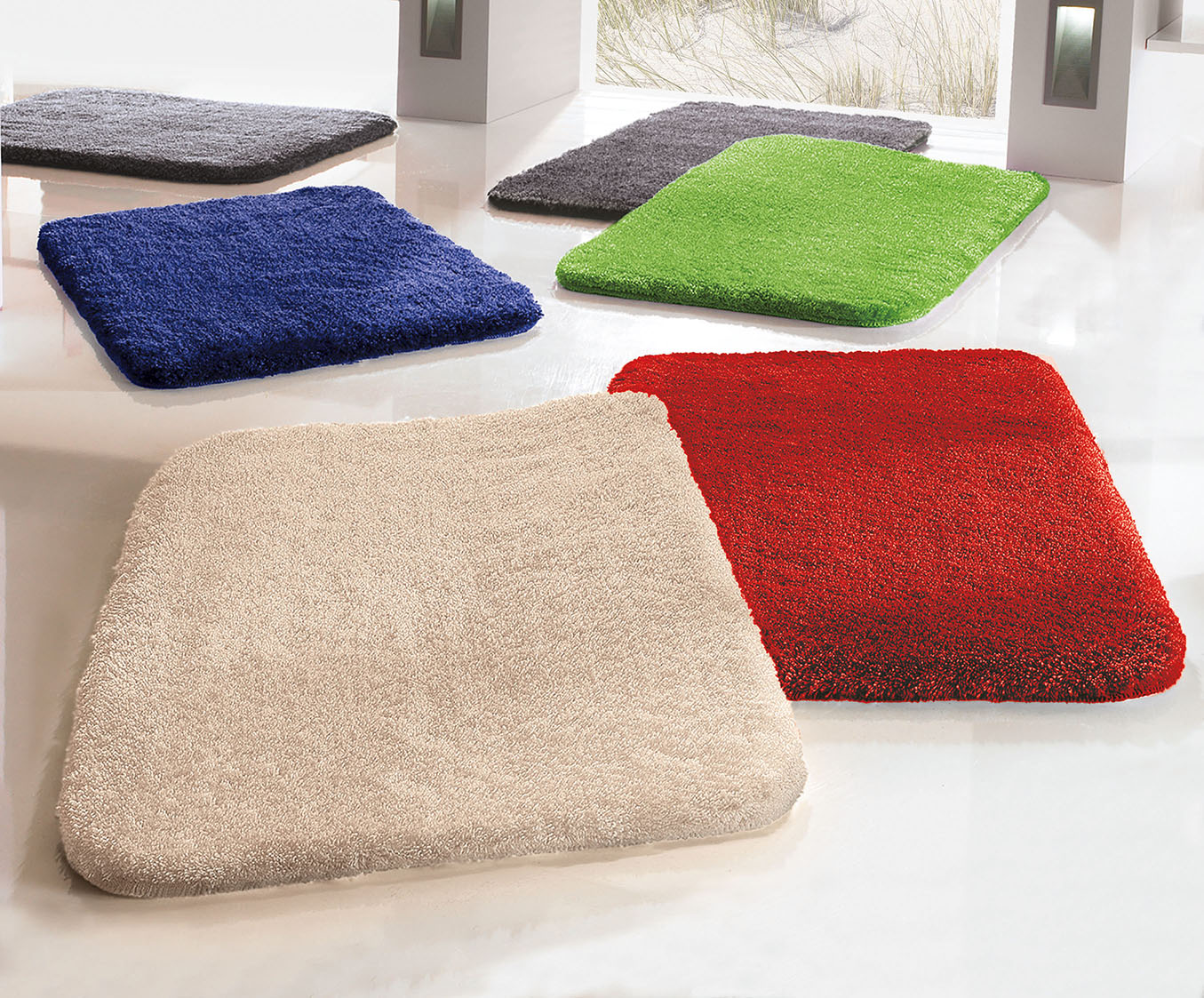 Weiche, rechteckige Badematten in verschiedenen Farben (blau, grün, grau, beige, rot) auf einem hellen Boden.
