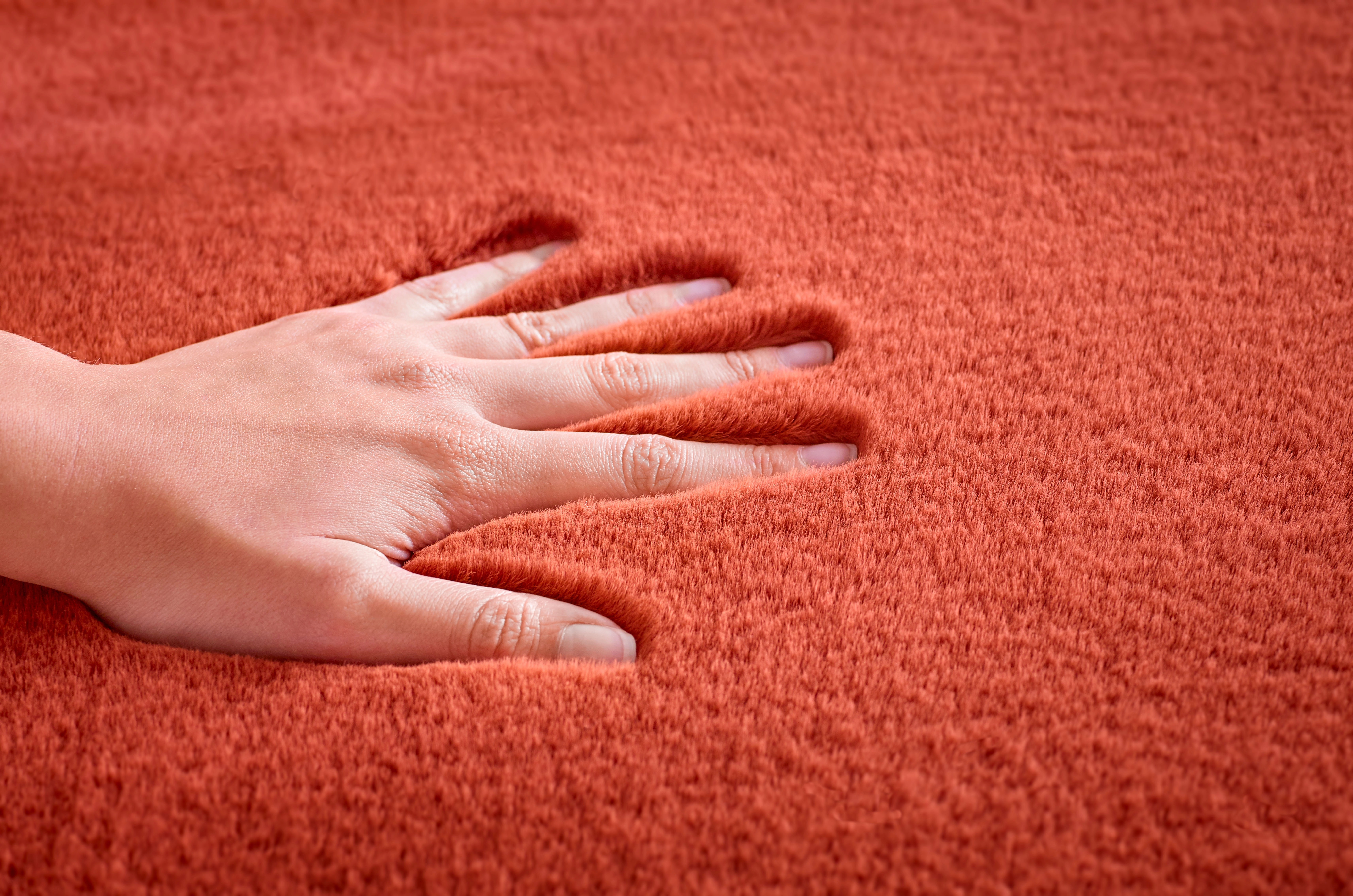 Weicher, roter Teppich mit Handabdruck, der die flauschige Textur und die hohe Qualität des Materials zeigt.