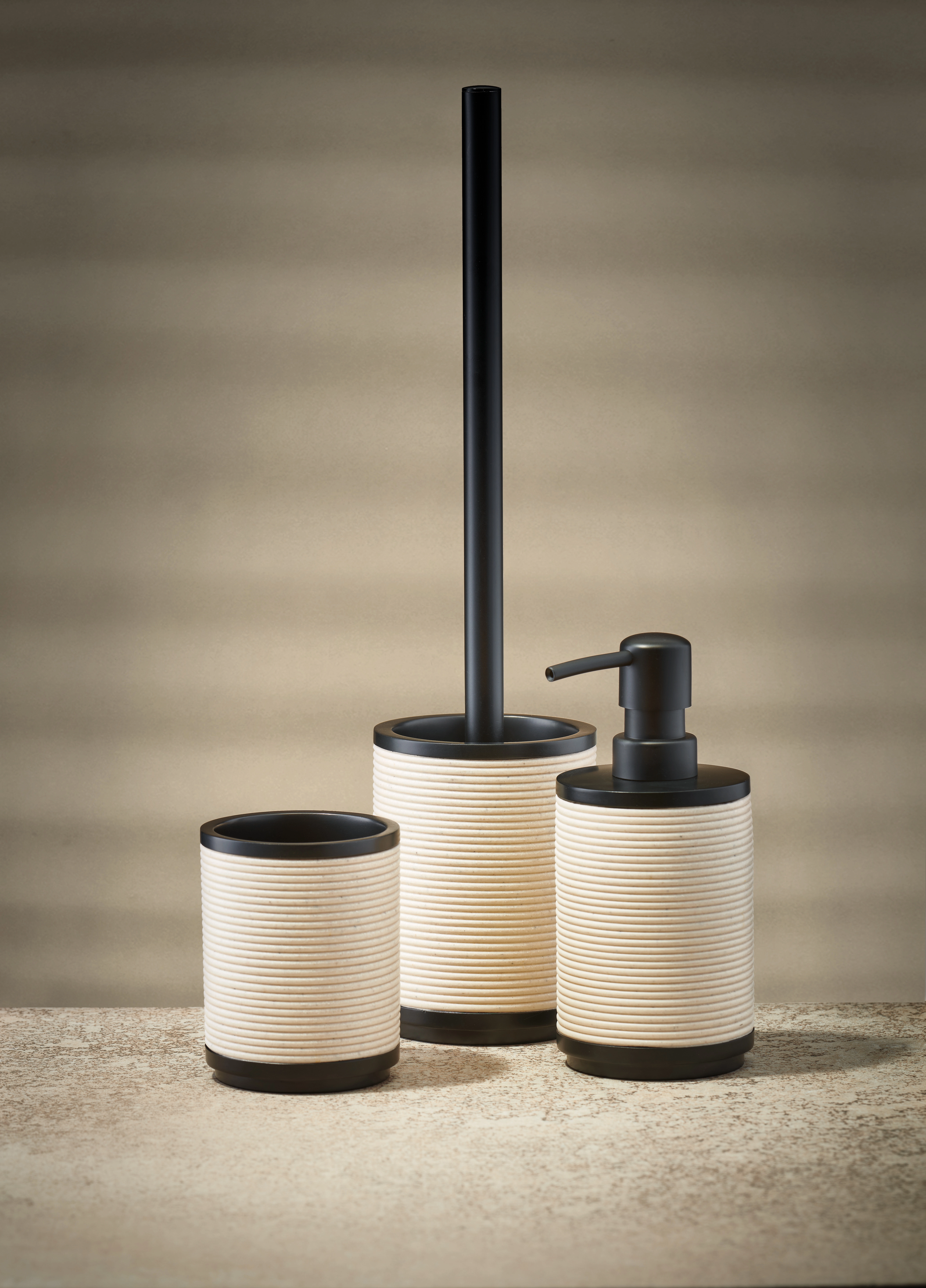 Badezimmer-Set in Beige und Schwarz, bestehend aus Seifenspender, Zahnbürstenhalter und WC-Bürste.