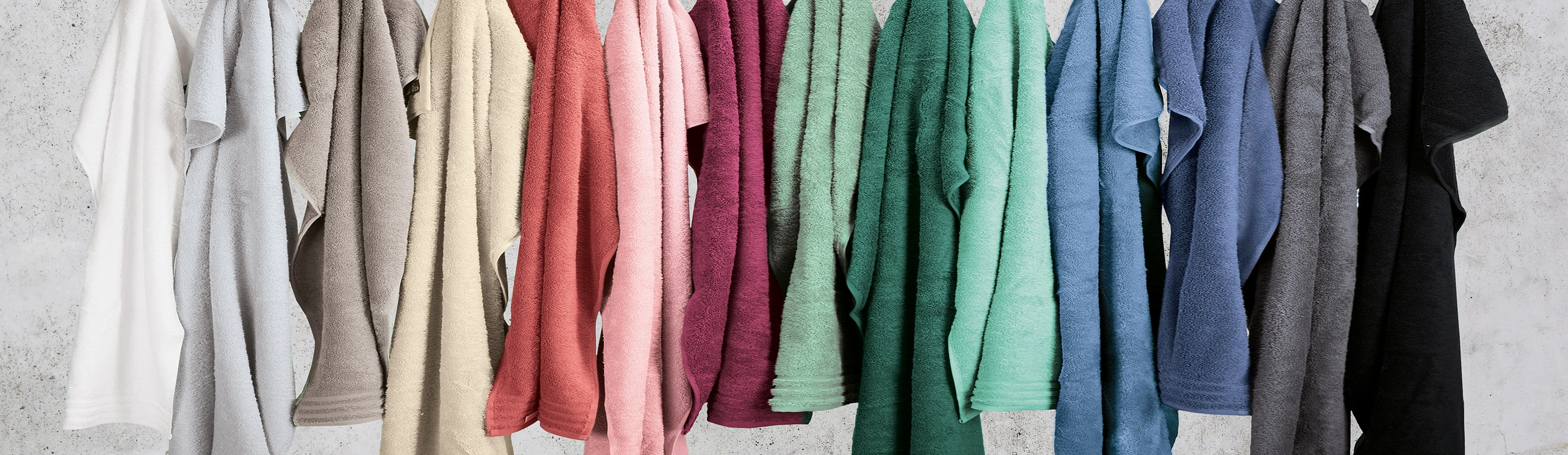 Bunte Handtücher in verschiedenen Farben, ordentlich nebeneinander an einer Wand aufgehängt.