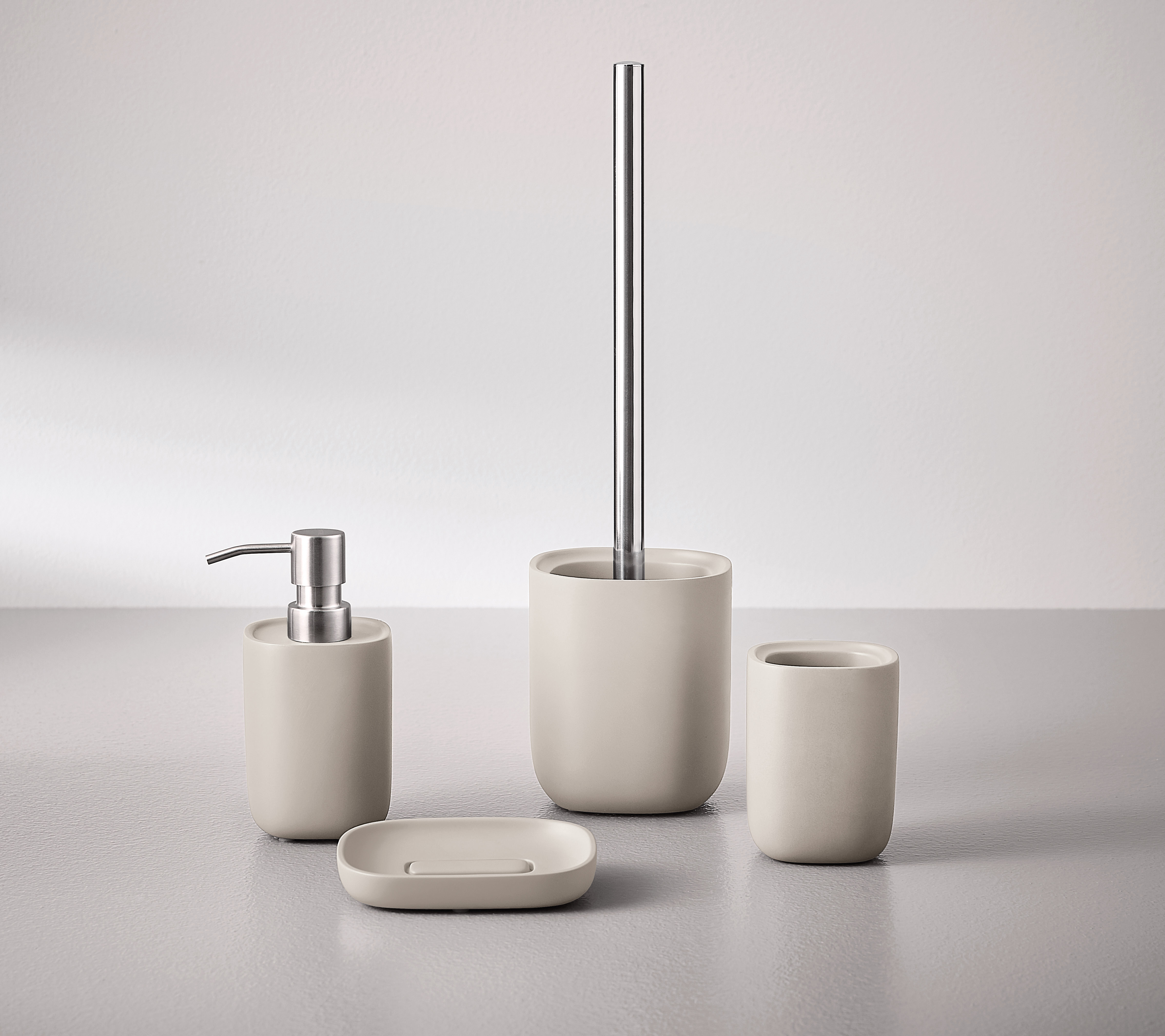 Beiges Badezimmer-Set aus Keramik mit Seifenspender, Zahnbürstenhalter, Seifenschale und WC-Bürste in modernem Design.