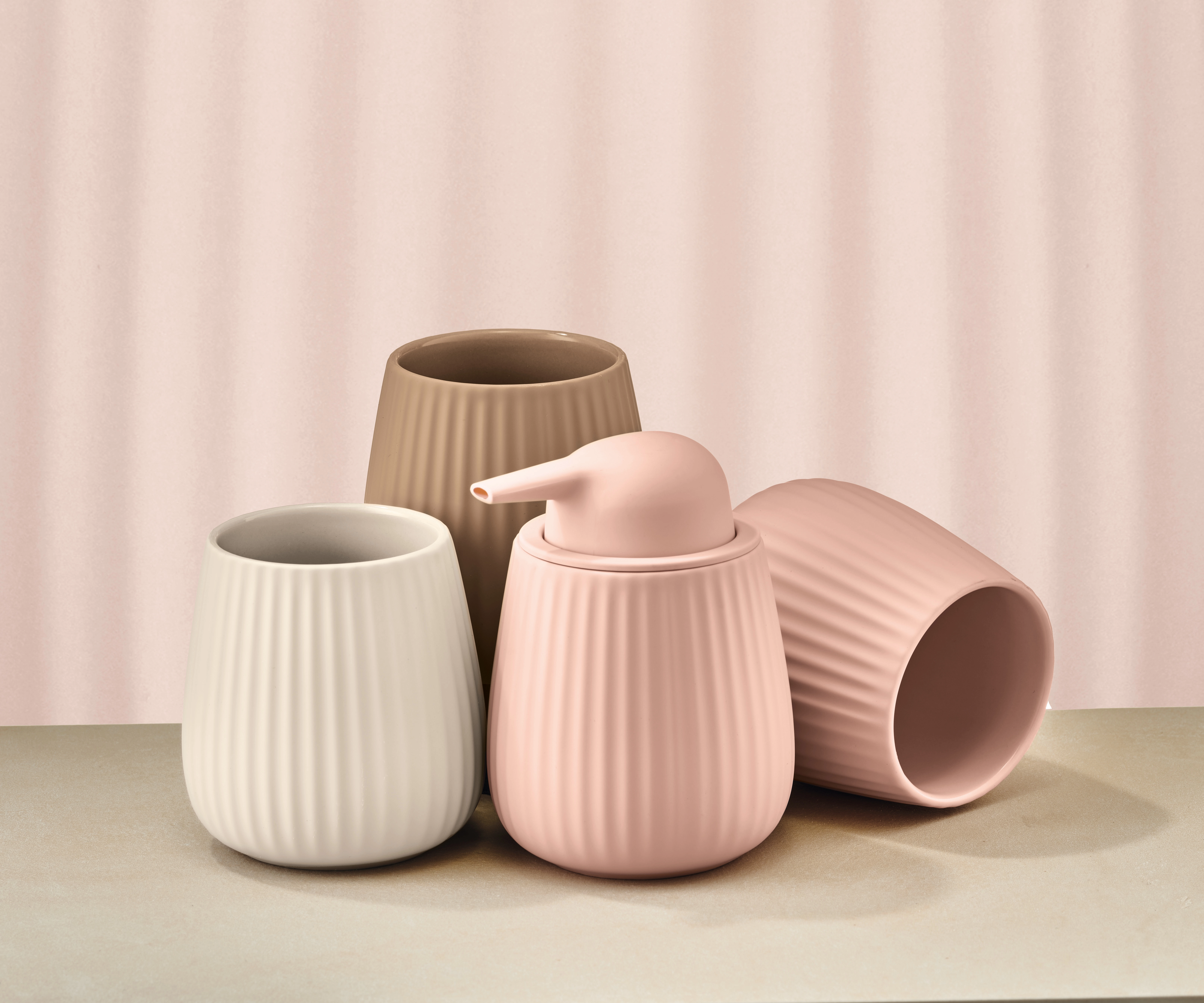 Set aus vier gerippten Badaccessoires in Beige, Weiß und Rosa, bestehend aus Seifenspender und Bechern.