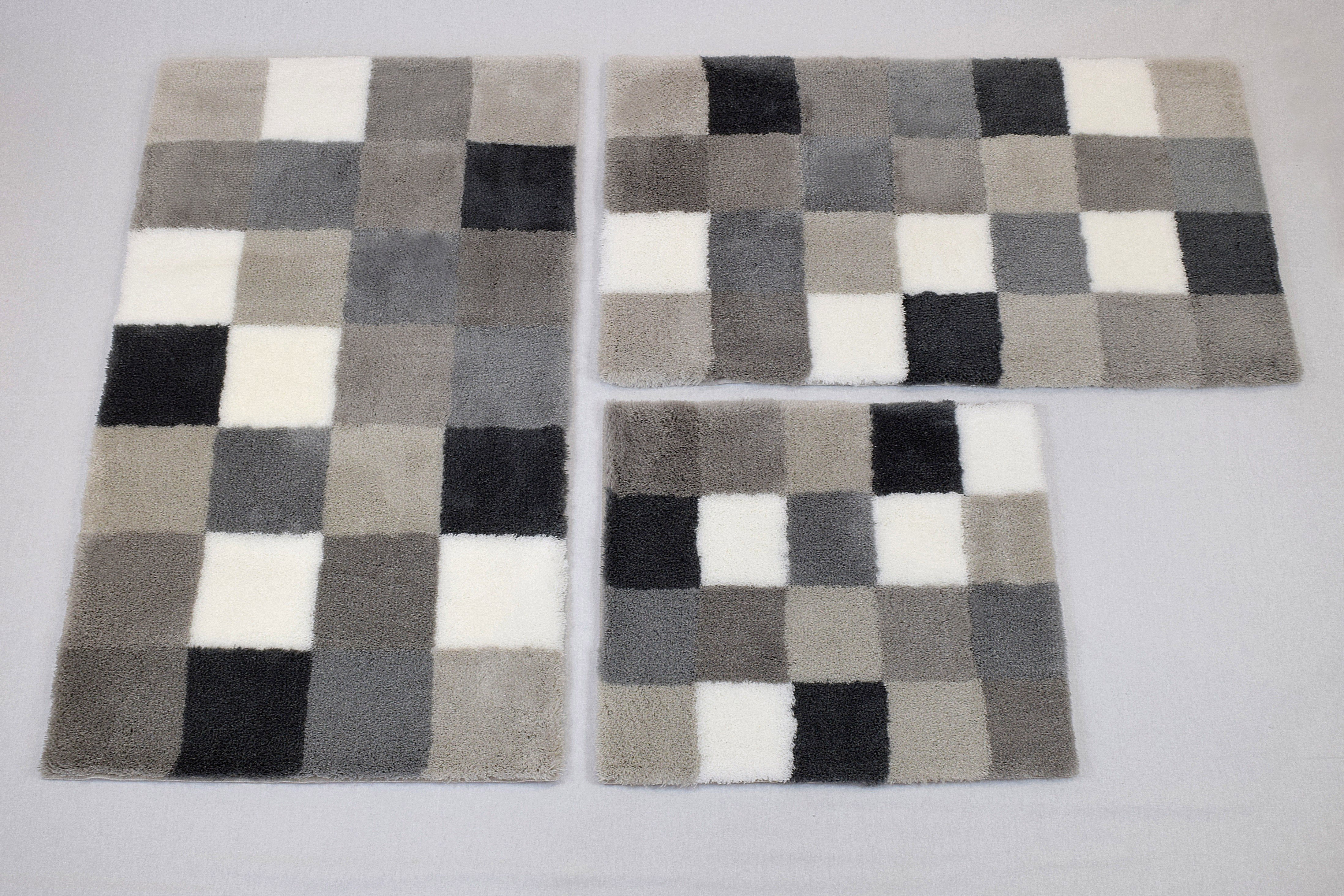 Drei rechteckige Teppiche in verschiedenen Größen mit einem modernen, grauen und weißen Karomuster auf einem hellen Hintergrund.