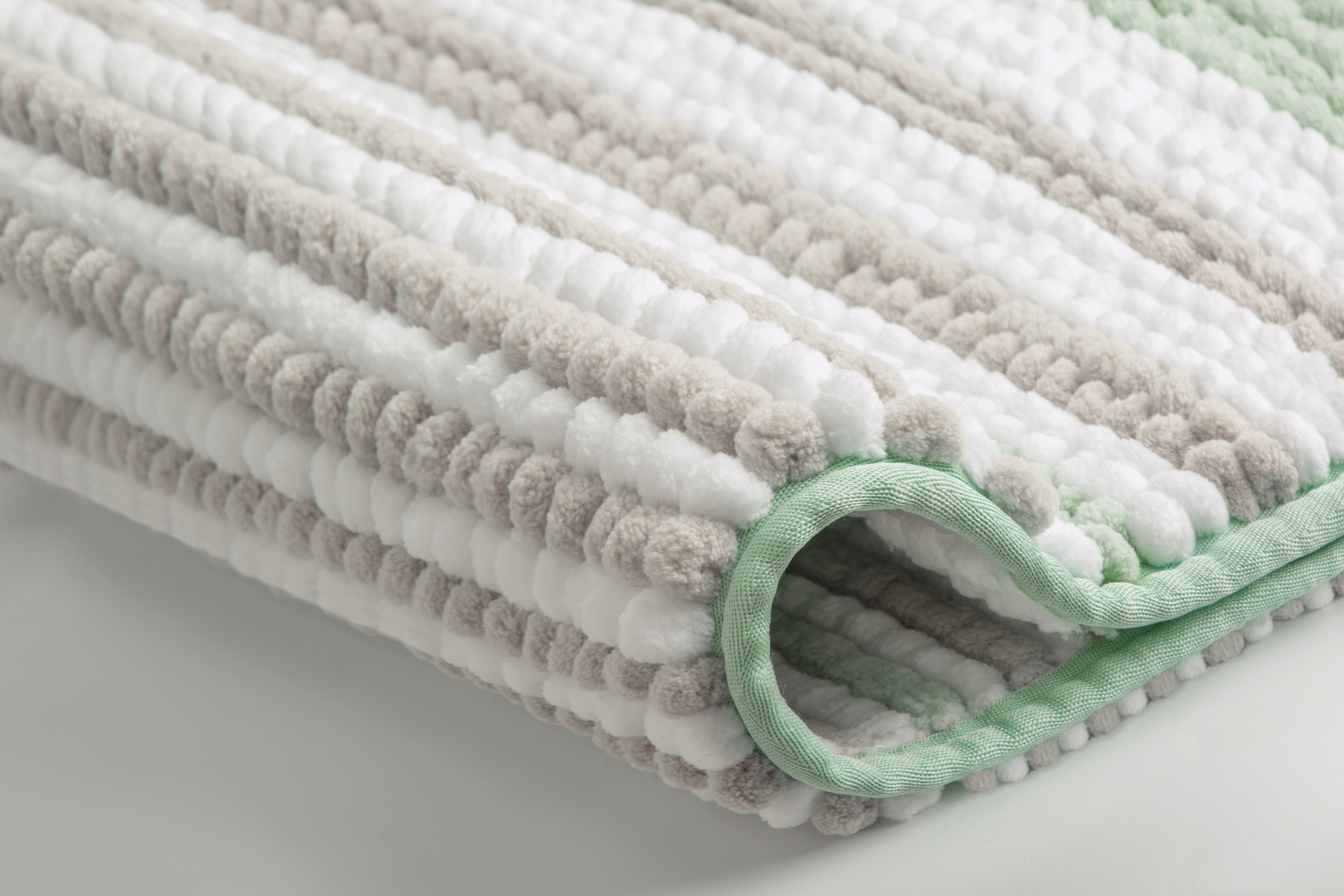 Weiche Badematte mit Streifenmuster in Weiß, Grau und Grün, detailreiche Nahaufnahme der Textur.